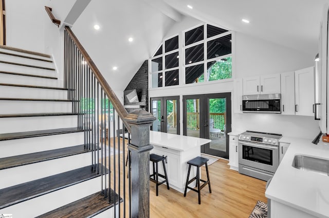 kitchen featuring light wood finished floors, stainless steel appliances, light countertops, white cabinets, and a kitchen bar