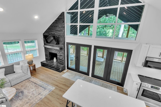 living room with light wood-style floors, high vaulted ceiling, french doors, and a stone fireplace