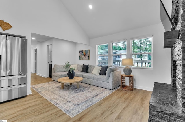 living area featuring light wood finished floors, baseboards, high vaulted ceiling, and a stone fireplace