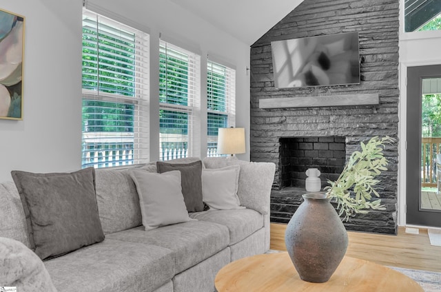 living room with a wealth of natural light, vaulted ceiling, wood finished floors, and a stone fireplace