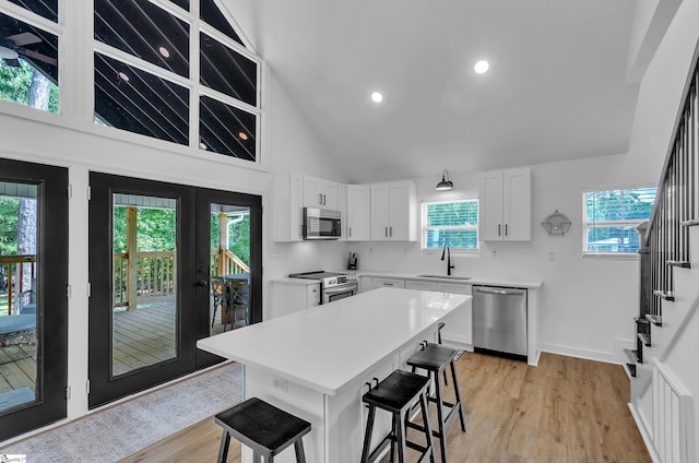 kitchen with a breakfast bar, appliances with stainless steel finishes, white cabinetry, a kitchen island, and a sink