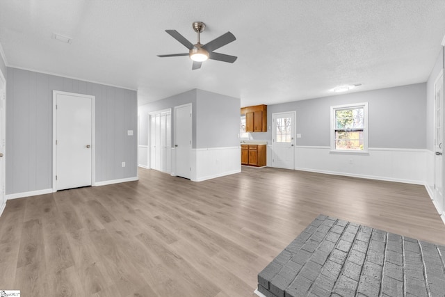 unfurnished living room with a ceiling fan, light wood-style flooring, and a textured ceiling