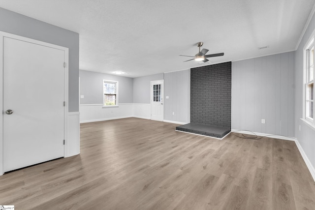 unfurnished living room featuring ceiling fan, a textured ceiling, a brick fireplace, and light wood-style floors