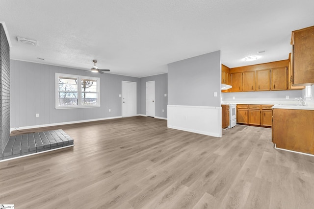 unfurnished living room featuring light wood-style flooring, a sink, a textured ceiling, ceiling fan, and baseboards