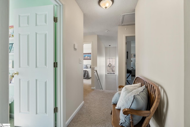 hallway with a textured ceiling, an upstairs landing, baseboards, carpet, and attic access