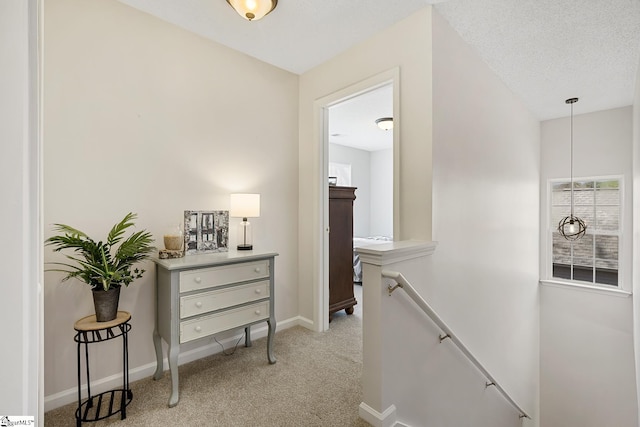 hall with baseboards, a textured ceiling, an upstairs landing, and light colored carpet