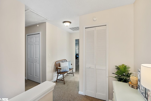 hallway with carpet, visible vents, attic access, a textured ceiling, and baseboards