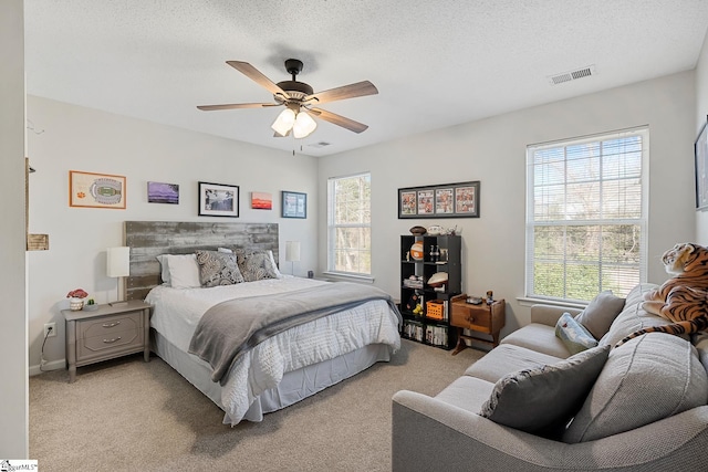 bedroom with light colored carpet, visible vents, ceiling fan, and a textured ceiling