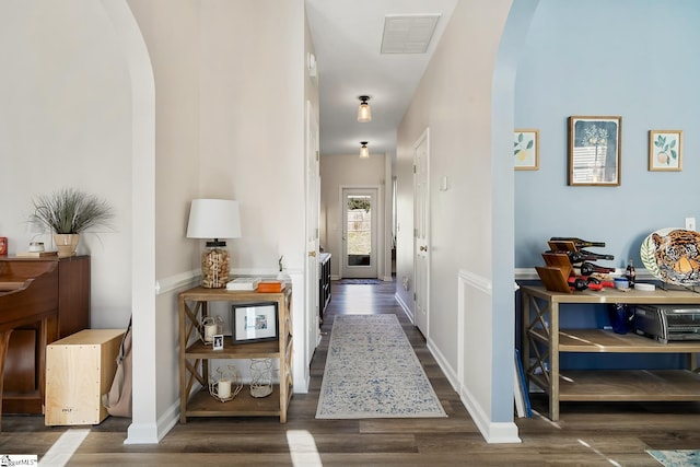 corridor featuring baseboards, visible vents, arched walkways, and dark wood-type flooring