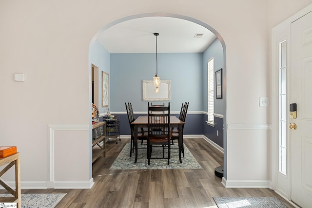 dining area featuring arched walkways, dark wood-style flooring, and visible vents