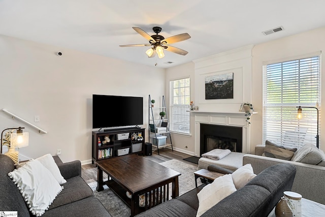 living area with ceiling fan, a fireplace, wood finished floors, and visible vents