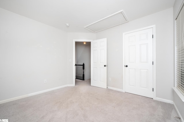 unfurnished bedroom featuring light carpet, attic access, and baseboards