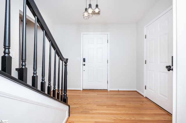 entryway with stairs, a chandelier, baseboards, and wood finished floors