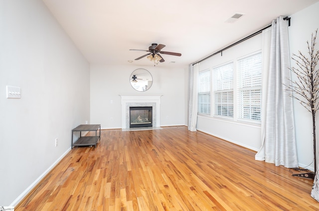 unfurnished living room featuring light wood finished floors, visible vents, baseboards, a fireplace with flush hearth, and ceiling fan