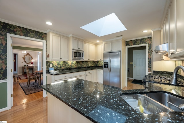 kitchen with a skylight, white cabinets, ornamental molding, stainless steel appliances, and a sink