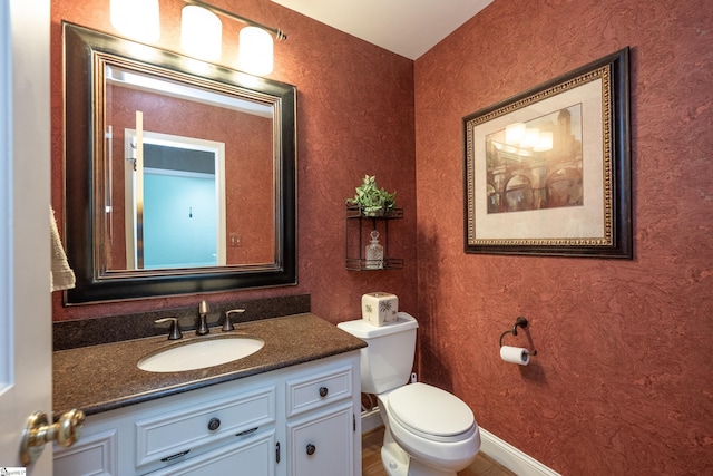 half bath featuring toilet, baseboards, and vanity