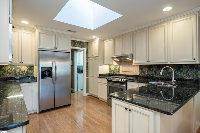 kitchen with a sink, under cabinet range hood, stainless steel appliances, and dark stone countertops