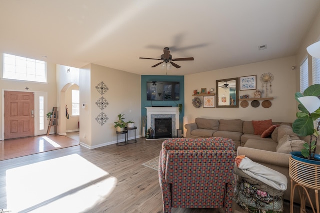 living room with light wood finished floors, baseboards, visible vents, arched walkways, and a glass covered fireplace