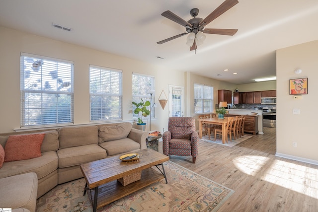 living area with light wood finished floors, baseboards, visible vents, and ceiling fan