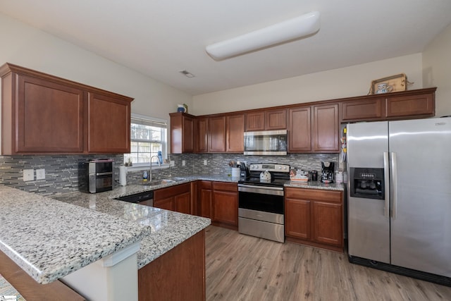 kitchen with a peninsula, a sink, light wood-style floors, appliances with stainless steel finishes, and light stone countertops