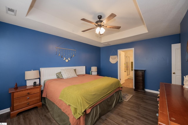 bedroom with ensuite bathroom, dark wood-style flooring, visible vents, baseboards, and a tray ceiling