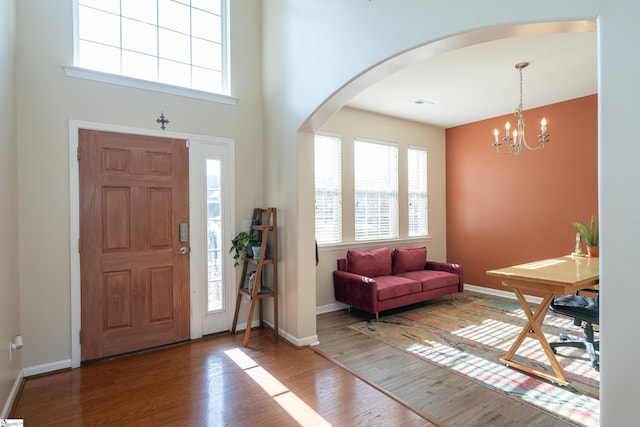 entrance foyer featuring an inviting chandelier, baseboards, arched walkways, and wood finished floors