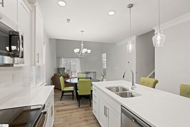 kitchen with white cabinets, appliances with stainless steel finishes, light countertops, pendant lighting, and a sink