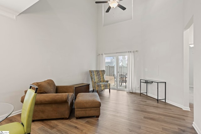 sitting room with light wood-type flooring, a towering ceiling, baseboards, and a ceiling fan