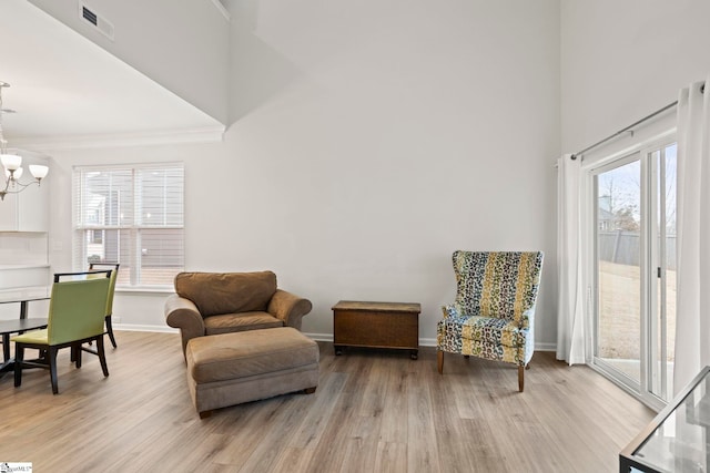 living area with a chandelier, light wood-type flooring, a towering ceiling, and baseboards