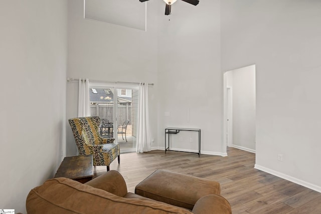 living area featuring a high ceiling, a ceiling fan, light wood-style flooring, and baseboards