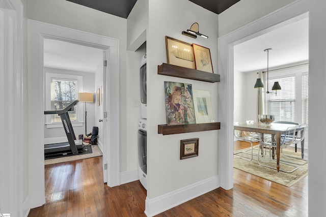 corridor featuring baseboards, dark wood-style flooring, and stacked washer / drying machine