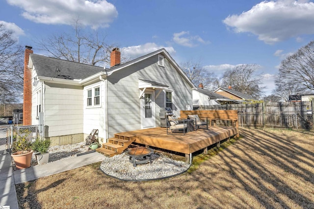 back of house with a wooden deck, a fire pit, a chimney, fence, and a yard