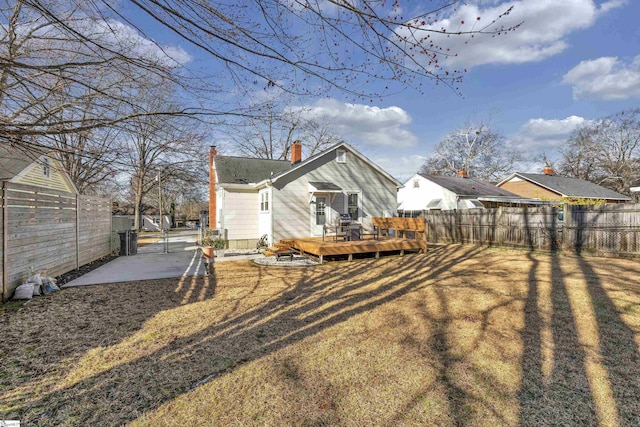 rear view of property featuring a fenced backyard, a yard, a wooden deck, a gate, and a chimney