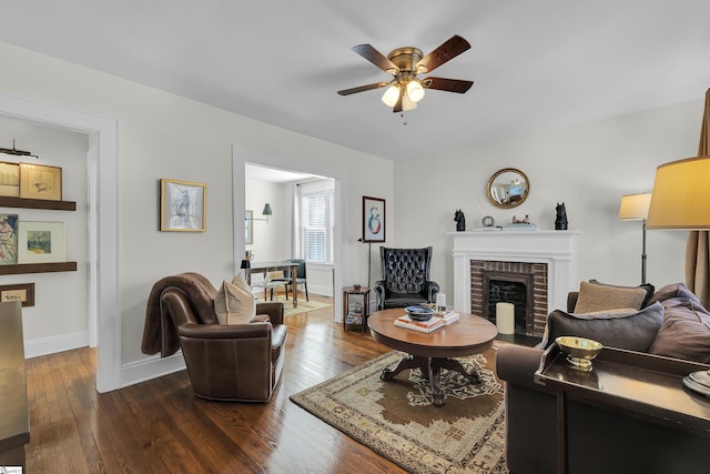 living room featuring dark wood-type flooring, a brick fireplace, a ceiling fan, and baseboards