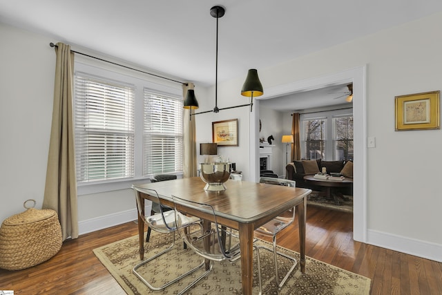 dining space featuring dark wood-type flooring, a wealth of natural light, a fireplace, and baseboards