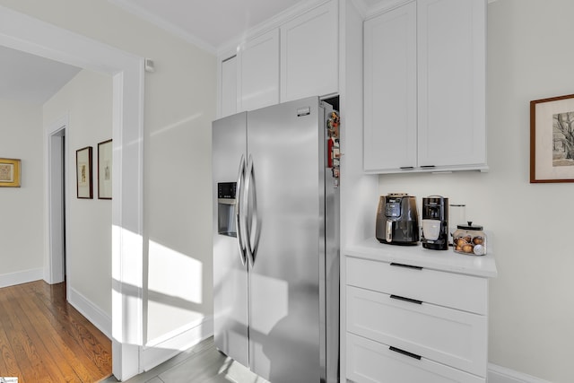 kitchen featuring light countertops, white cabinetry, light wood-type flooring, stainless steel fridge, and baseboards