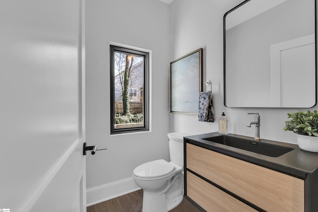 half bathroom featuring toilet, wood finished floors, vanity, and baseboards