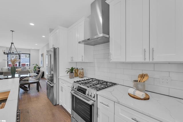 kitchen with stainless steel appliances, white cabinets, hanging light fixtures, light stone countertops, and wall chimney exhaust hood