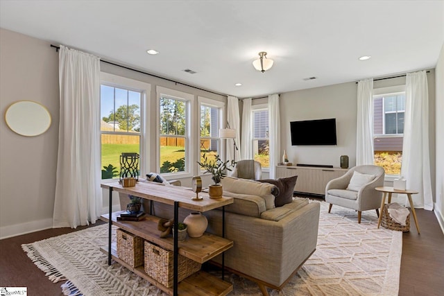 living area with a wealth of natural light, visible vents, baseboards, and wood finished floors