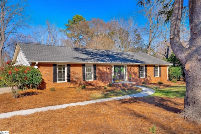 ranch-style home featuring brick siding, a front lawn, and roof with shingles