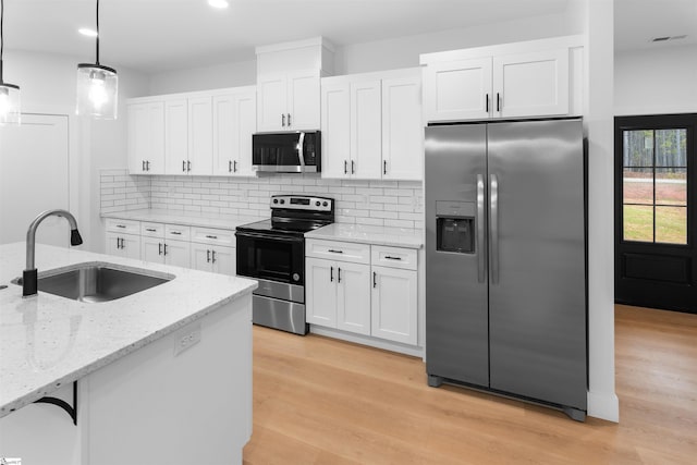 kitchen featuring stainless steel appliances, a sink, white cabinetry, light stone countertops, and pendant lighting