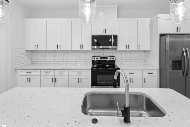 kitchen with appliances with stainless steel finishes, a sink, light stone counters, and white cabinets