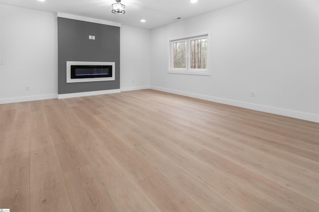 unfurnished living room featuring light wood-type flooring, a glass covered fireplace, and baseboards