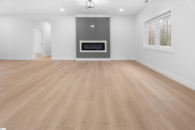 unfurnished living room with recessed lighting, a glass covered fireplace, light wood-style flooring, and baseboards