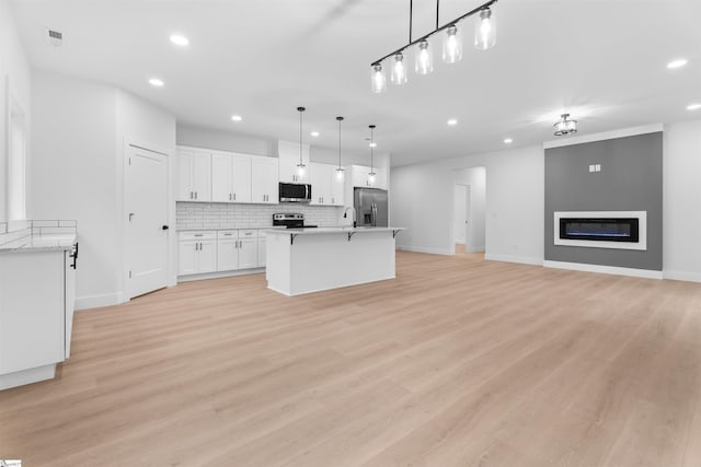 kitchen with appliances with stainless steel finishes, open floor plan, light countertops, white cabinetry, and pendant lighting