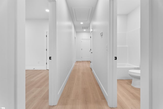 hallway with light wood-type flooring, attic access, visible vents, and baseboards