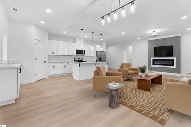 living room with a glass covered fireplace, baseboards, light wood finished floors, and recessed lighting