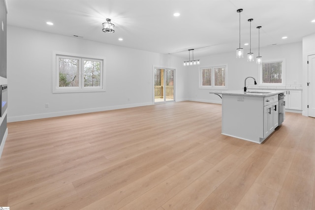 kitchen featuring open floor plan, a sink, hanging light fixtures, and a center island with sink