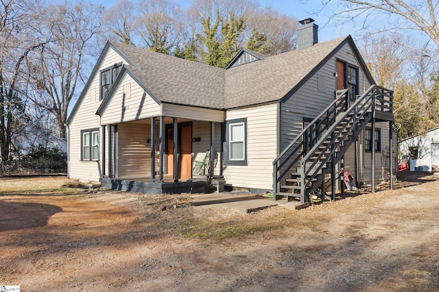 view of front of house featuring a shingled roof, a chimney, covered porch, and stairway