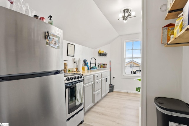 kitchen featuring lofted ceiling, light wood-style flooring, stainless steel appliances, a sink, and light countertops